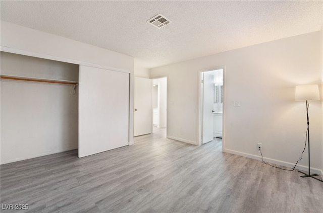 unfurnished bedroom with a textured ceiling, light wood-style flooring, visible vents, baseboards, and a closet