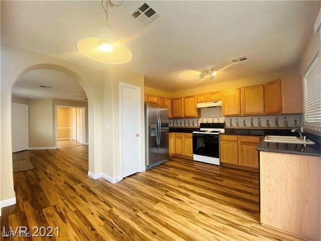 kitchen featuring wood-type flooring, stove, sink, and stainless steel fridge