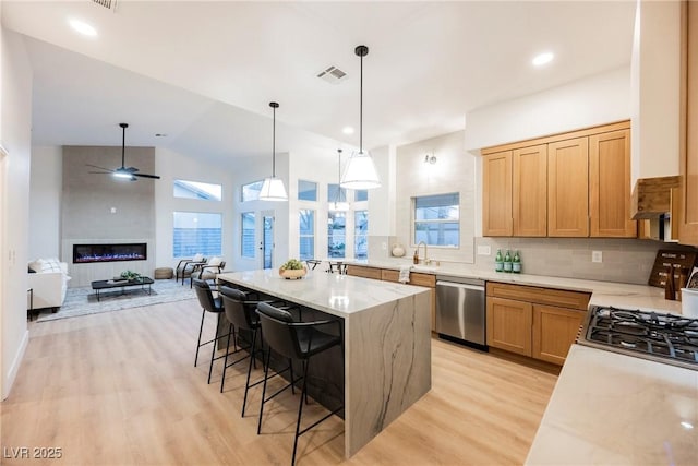 kitchen with a breakfast bar area, backsplash, stainless steel appliances, decorative light fixtures, and light wood-type flooring