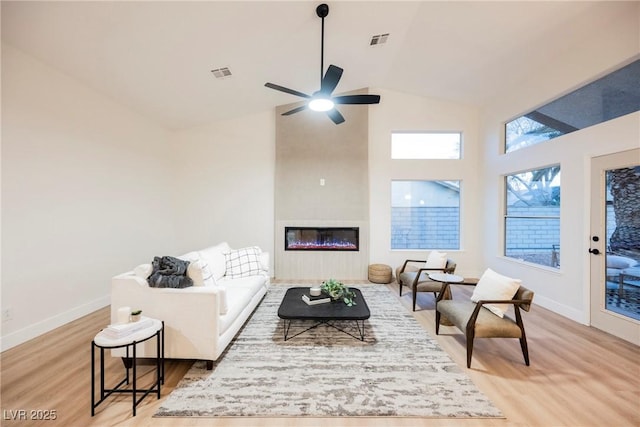 living room featuring ceiling fan, high vaulted ceiling, a large fireplace, and light hardwood / wood-style floors