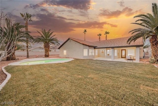 back house at dusk featuring a patio and a lawn