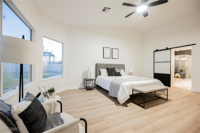 bedroom with light hardwood / wood-style flooring, a barn door, ceiling fan, and vaulted ceiling