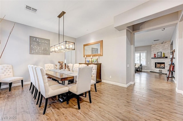 dining space with light wood-type flooring, a chandelier, and a stone fireplace