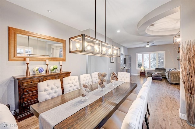 dining space featuring light hardwood / wood-style floors, ceiling fan, and a tray ceiling