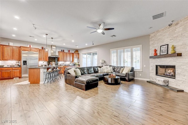 living room featuring light hardwood / wood-style flooring, ceiling fan, and a stone fireplace