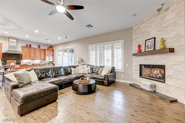 living room featuring a fireplace, ceiling fan, and light hardwood / wood-style floors