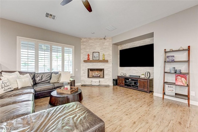 living room with a fireplace, ceiling fan, and light wood-type flooring