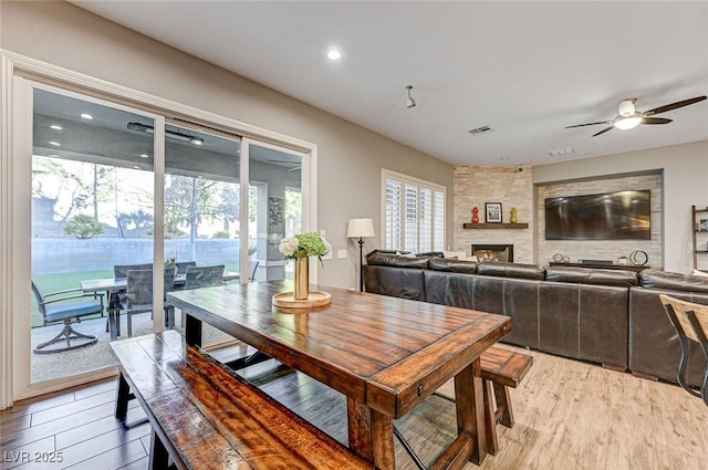 dining room with light wood-type flooring, ceiling fan, and a fireplace