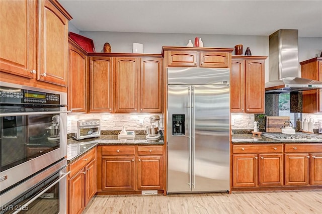 kitchen featuring light hardwood / wood-style flooring, stainless steel appliances, dark stone counters, and wall chimney range hood