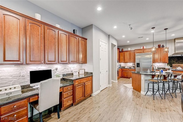 kitchen with stainless steel built in refrigerator, built in desk, wall chimney exhaust hood, light hardwood / wood-style floors, and sink