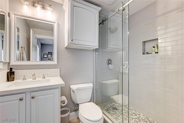 bathroom with toilet, a shower with shower door, and vanity