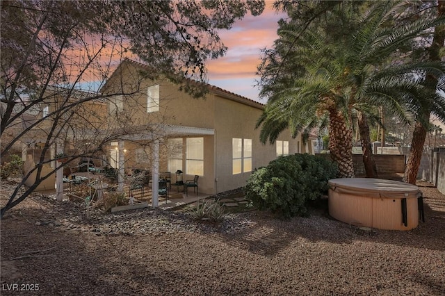 property exterior at dusk featuring a hot tub and a patio