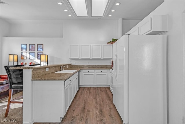 kitchen with sink, a breakfast bar, white refrigerator, white cabinets, and kitchen peninsula