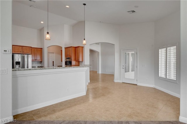 kitchen featuring pendant lighting, appliances with stainless steel finishes, high vaulted ceiling, light stone counters, and kitchen peninsula