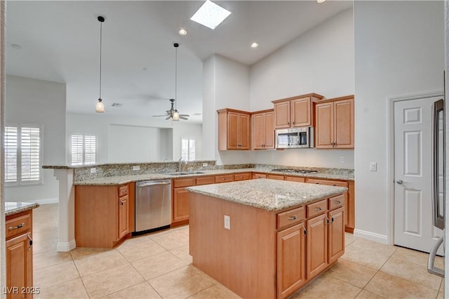 kitchen with pendant lighting, sink, appliances with stainless steel finishes, a center island, and light stone countertops