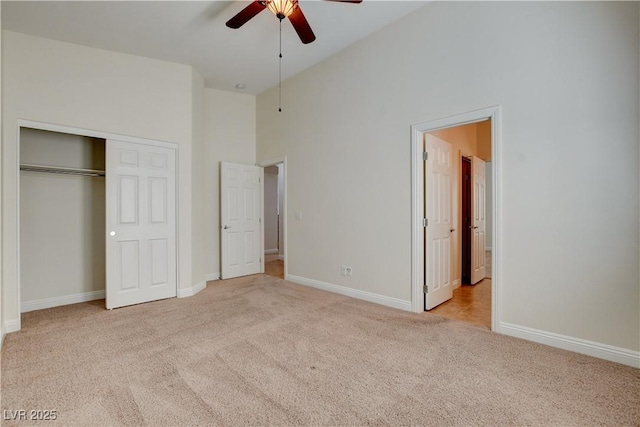 unfurnished bedroom with ceiling fan, a closet, high vaulted ceiling, and light carpet