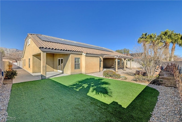 rear view of house with a yard, a patio, and solar panels