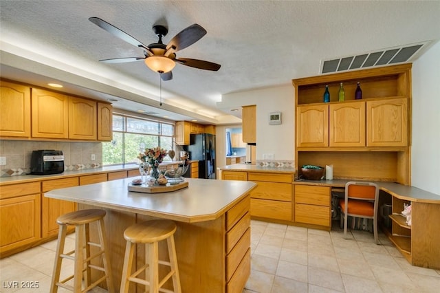 kitchen featuring a breakfast bar area, black fridge, a center island, built in desk, and decorative backsplash