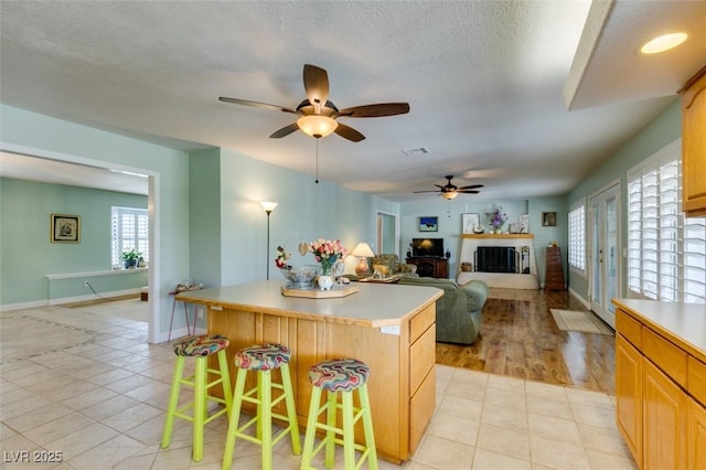 kitchen featuring light tile patterned flooring, a breakfast bar, a center island, a textured ceiling, and light brown cabinets