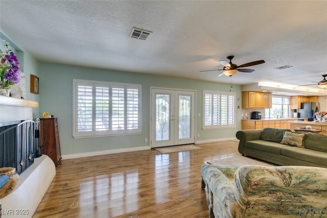 living room featuring ceiling fan, a textured ceiling, light hardwood / wood-style floors, and french doors