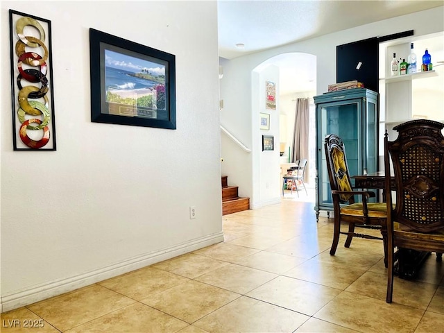 living area featuring stairs, arched walkways, baseboards, and light tile patterned floors