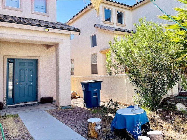 view of exterior entry with a tile roof, fence, and stucco siding