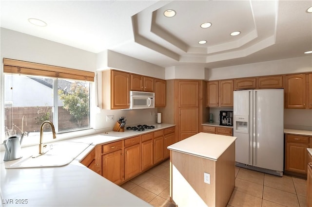 kitchen featuring white appliances, a center island, a tray ceiling, light countertops, and a sink