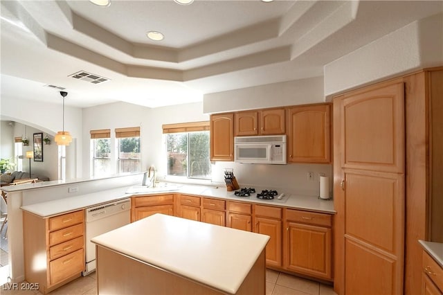 kitchen featuring white appliances, a raised ceiling, a sink, and a peninsula