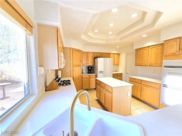 kitchen featuring a tray ceiling, white appliances, plenty of natural light, and a sink