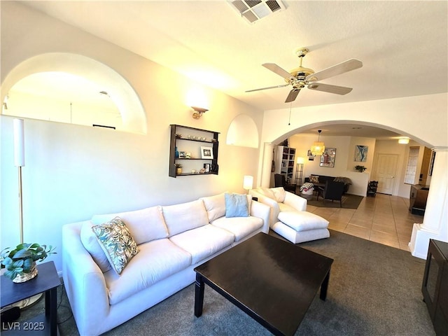 carpeted living room with tile patterned flooring, visible vents, arched walkways, and a ceiling fan