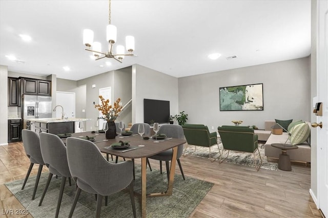 dining area with an inviting chandelier, sink, and light wood-type flooring