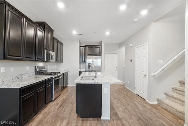 kitchen with appliances with stainless steel finishes, sink, a center island with sink, and light wood-type flooring