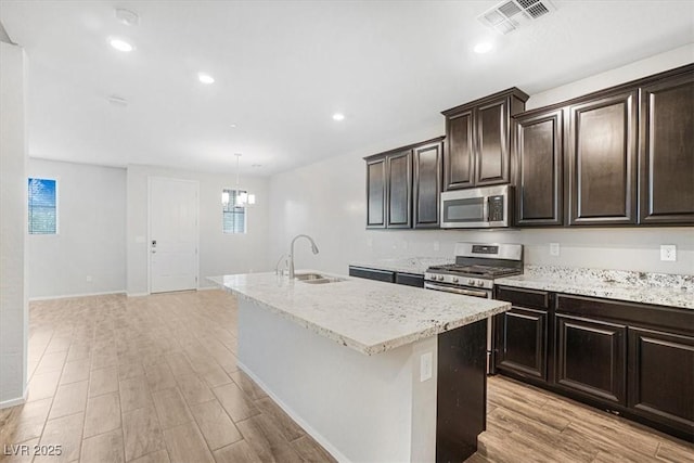 kitchen with sink, decorative light fixtures, light hardwood / wood-style flooring, stainless steel appliances, and a kitchen island with sink