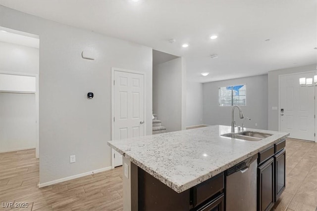 kitchen with sink, stainless steel dishwasher, dark brown cabinetry, a center island with sink, and light wood-type flooring