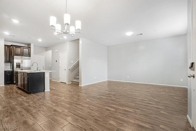 kitchen with sink, stainless steel fridge with ice dispenser, dark brown cabinets, dark hardwood / wood-style flooring, and an island with sink