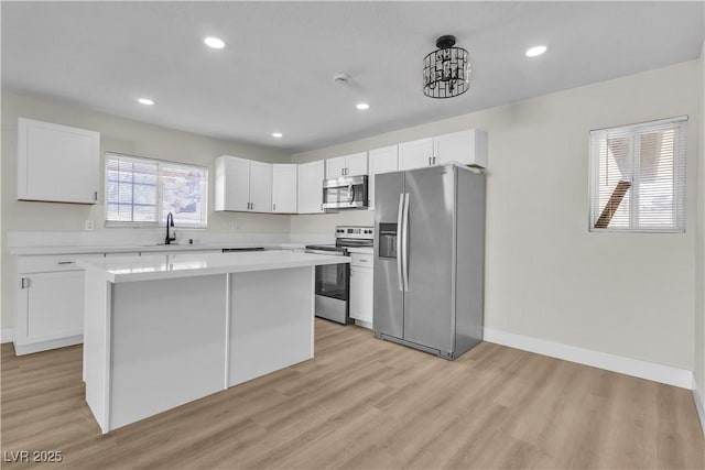 kitchen with sink, appliances with stainless steel finishes, white cabinetry, a kitchen island, and light wood-type flooring