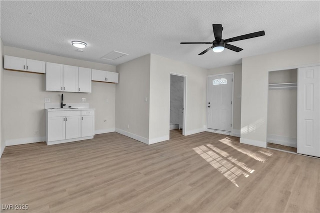 unfurnished living room featuring ceiling fan, sink, a textured ceiling, and light wood-type flooring