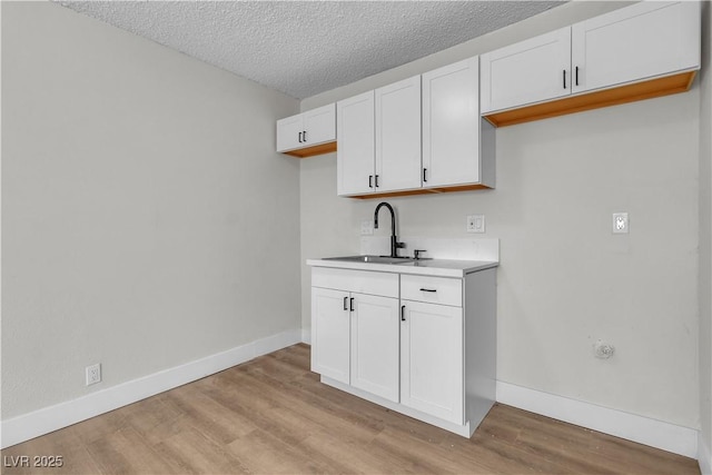 kitchen featuring white cabinetry, sink, light hardwood / wood-style floors, and a textured ceiling