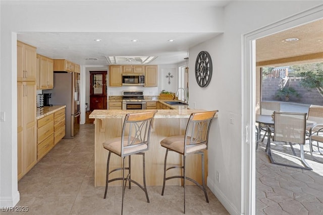 kitchen featuring light brown cabinetry, sink, a kitchen bar, kitchen peninsula, and stainless steel appliances