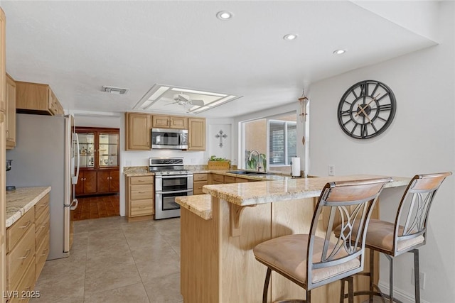 kitchen featuring sink, a kitchen bar, light stone counters, kitchen peninsula, and stainless steel appliances