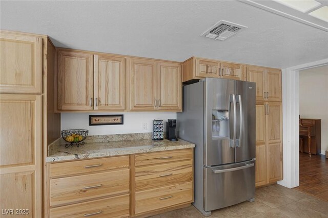 kitchen with stainless steel fridge, light stone countertops, and light brown cabinets