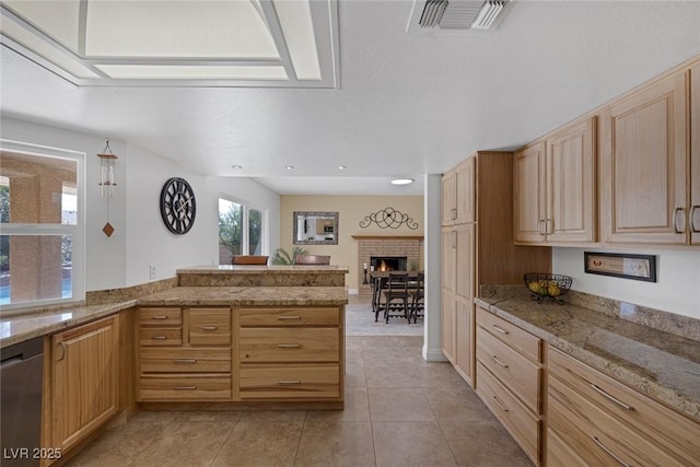 kitchen with light tile patterned floors, dishwasher, light brown cabinetry, a brick fireplace, and kitchen peninsula