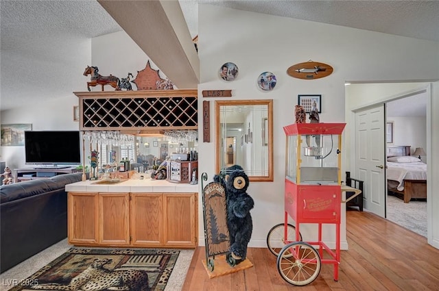 kitchen with tile countertops, light wood finished floors, open floor plan, and lofted ceiling