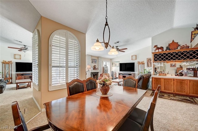 dining area featuring light carpet, visible vents, ceiling fan, vaulted ceiling, and a fireplace