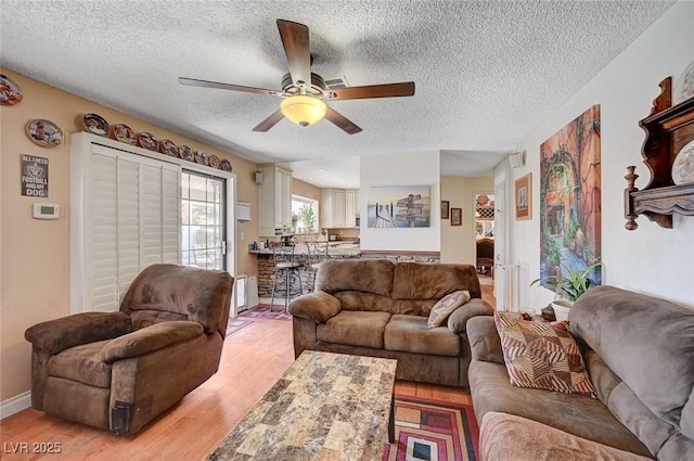 living room with light wood-style floors, ceiling fan, a textured ceiling, and baseboards