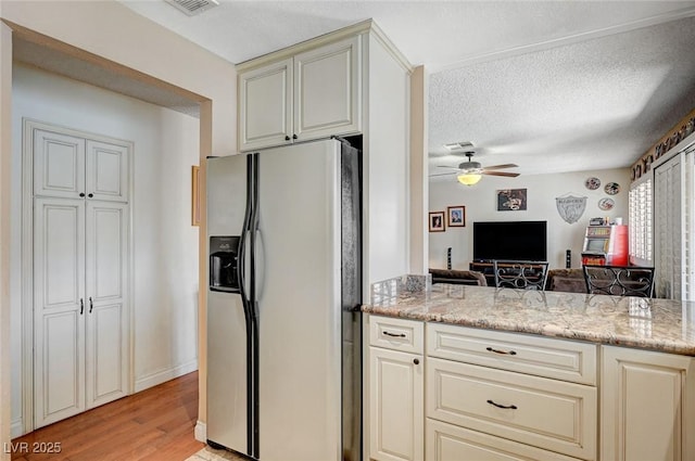 kitchen featuring a textured ceiling, cream cabinets, open floor plan, stainless steel refrigerator with ice dispenser, and light stone countertops