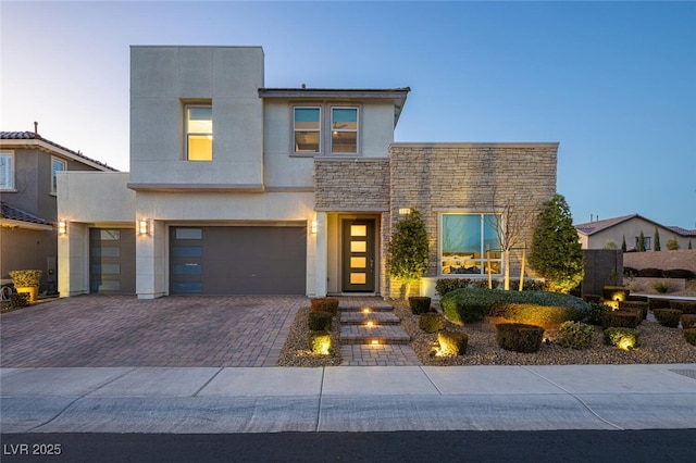 contemporary home featuring a garage, stone siding, decorative driveway, and stucco siding