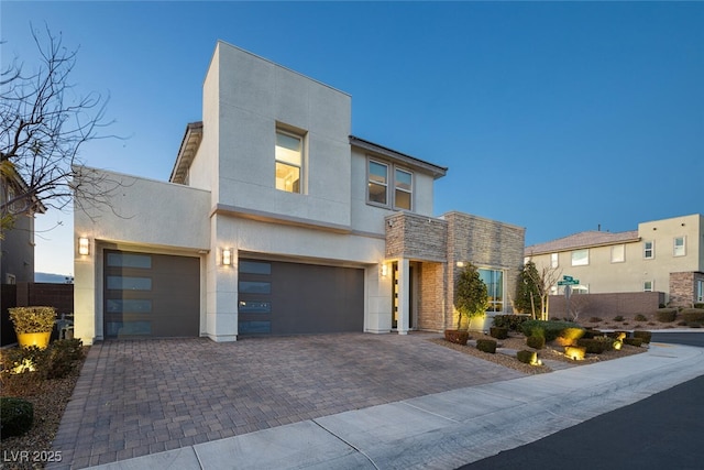 contemporary home with stone siding, decorative driveway, and stucco siding