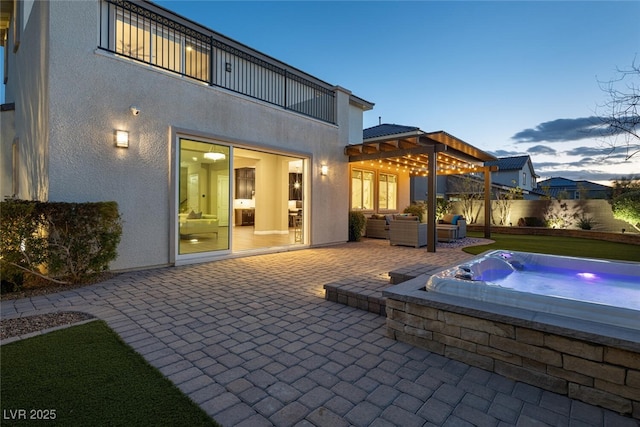 rear view of property with a balcony, an outdoor living space, an outdoor hot tub, stucco siding, and a patio area