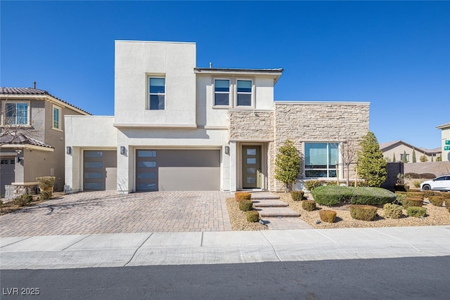 contemporary home with decorative driveway, stone siding, an attached garage, and stucco siding